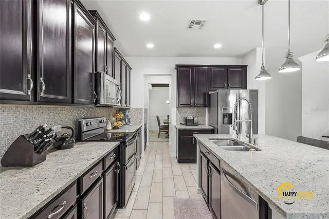 a open kitchen with stainless steel appliances granite countertop a stove top oven a sink dishwasher a dining table and chairs with wooden floor