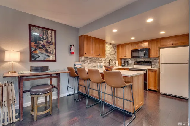 a kitchen with stainless steel appliances granite countertop a refrigerator a stove a sink a dining table and chairs with wooden floor