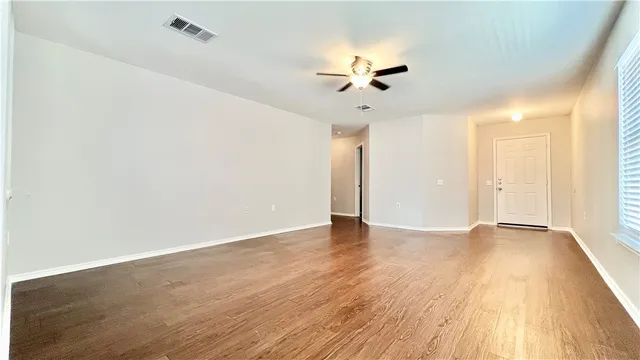 an empty room with wooden floor fan and windows