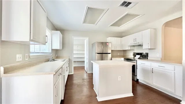a kitchen with stainless steel appliances a sink a stove a refrigerator cabinets and a window