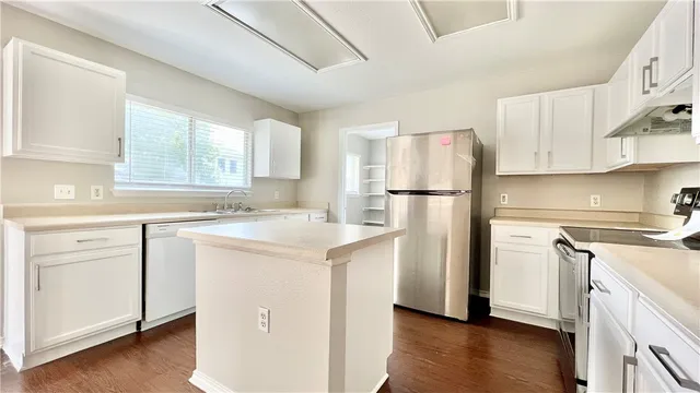 a kitchen with a refrigerator a stove a sink and white cabinets with wooden floor