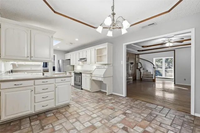 a open kitchen with a sink dishwasher a stove and white cabinets with wooden floor