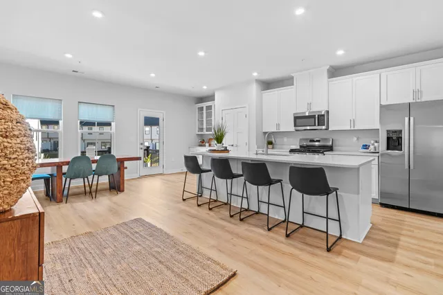 a kitchen with stainless steel appliances kitchen island granite countertop a stove a refrigerator a sink a dining table and chairs with wooden floor