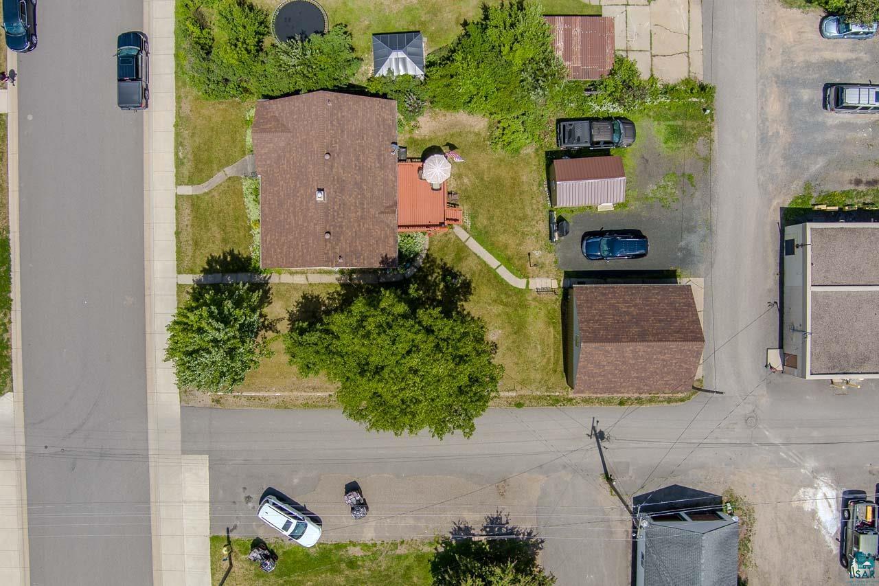 101 2nd Avenue North Biwabik, MN 55708 - Photo 44 of 44 Aerial view of property featuring a primary residence with a brown shingle roof, a detached garage with a brown shingle roof, a red-toned outdoor deck, a paved driveway, and mature trees