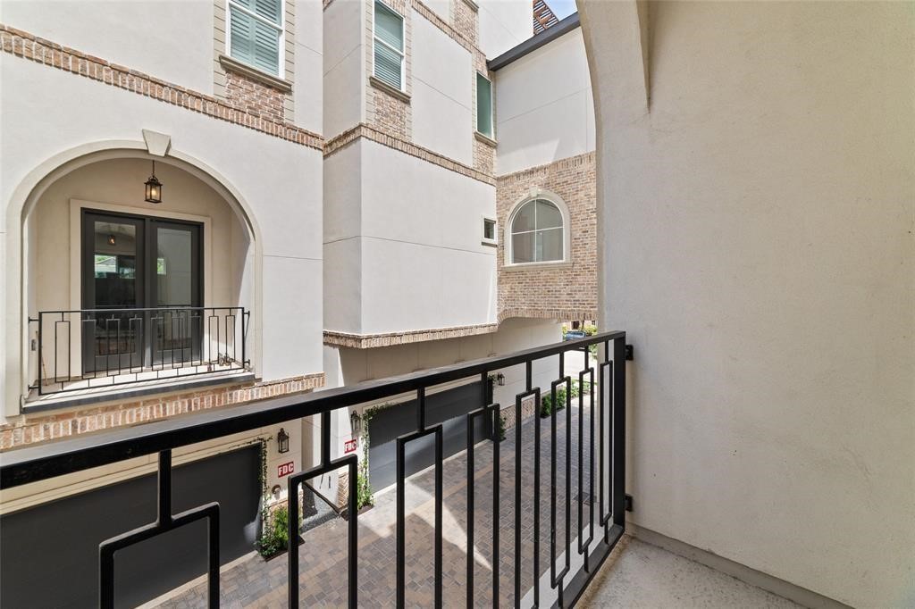 710 Delano Street, Unit A Houston, TX 77003 - Photo 25 of 32 This photo showcases a small balcony with a black metal railing, overlooking a courtyard area with brick and stucco building facades. The view includes arched windows and doors, adding a touch of architectural charm.