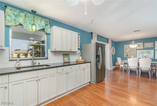 a kitchen with stainless steel appliances granite countertop a refrigerator a sink dishwasher and white cabinets with wooden floor