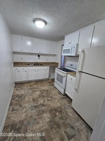 a kitchen with granite countertop a sink a stove a refrigerator and white cabinets