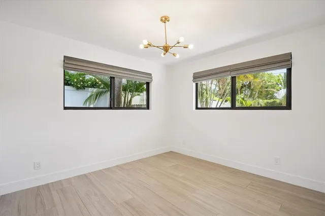 an empty room with wooden floor chandelier and windows