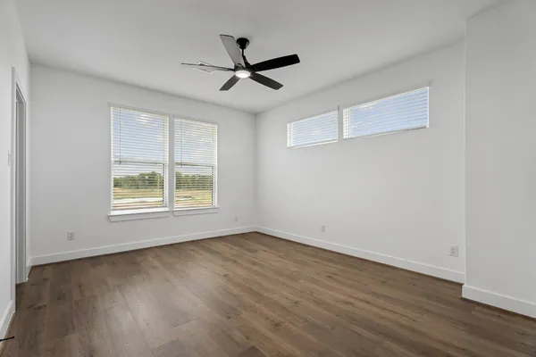 an empty room with wooden floor and a ceiling fan
