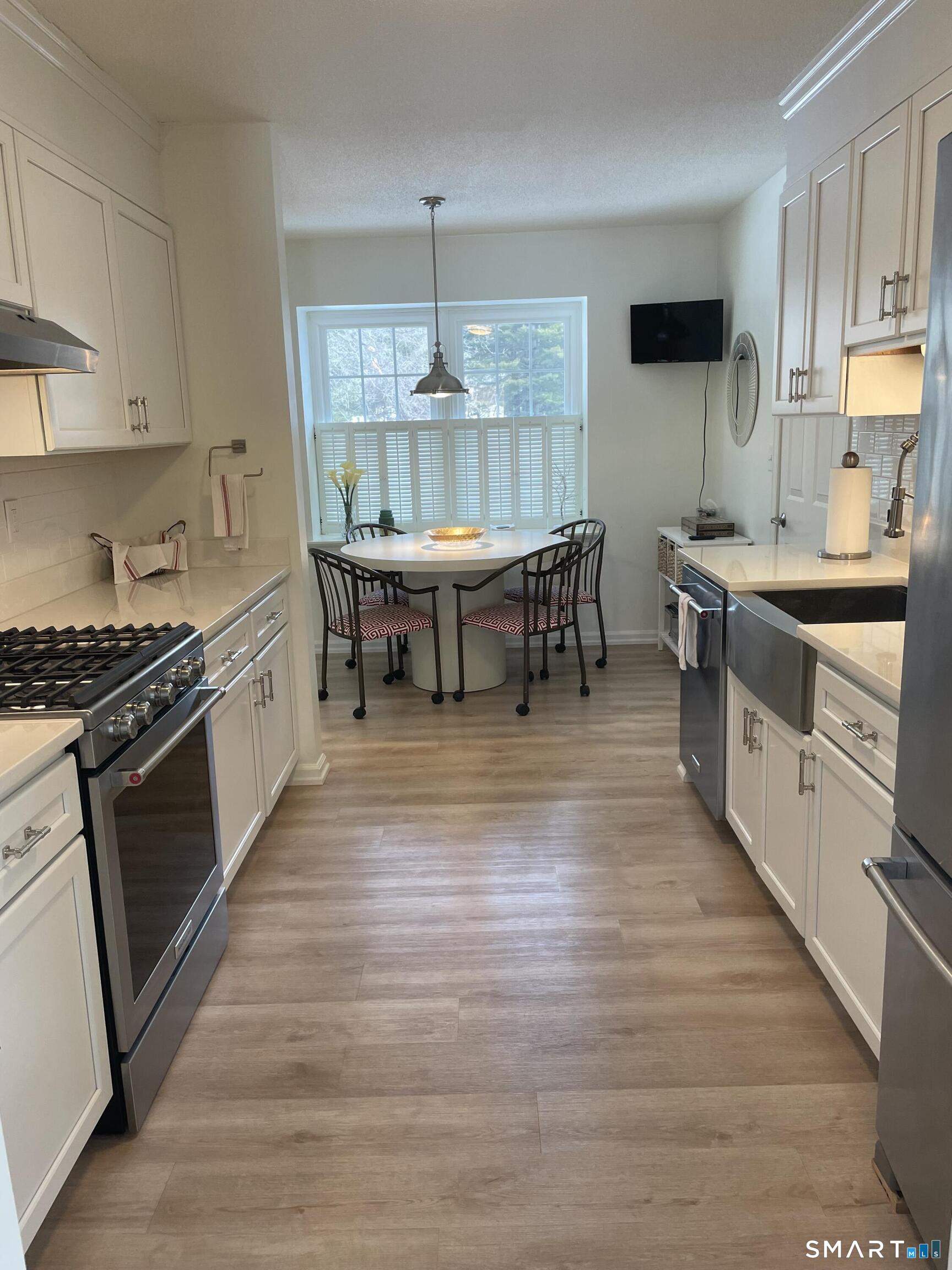 a kitchen with stainless steel appliances granite countertop a stove top oven a sink dishwasher and white cabinets with wooden floor