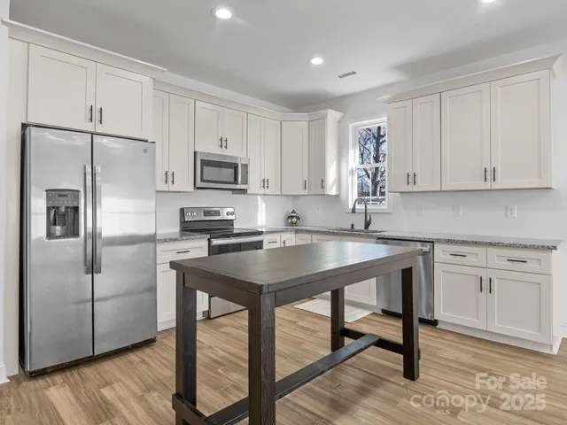 a kitchen with stainless steel appliances granite countertop a refrigerator a stove a sink and white cabinets with wooden floor