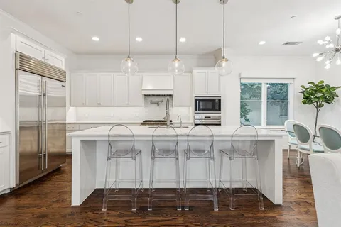 a large white kitchen with granite countertop a stove a sink a refrigerator and white cabinets with wooden floor