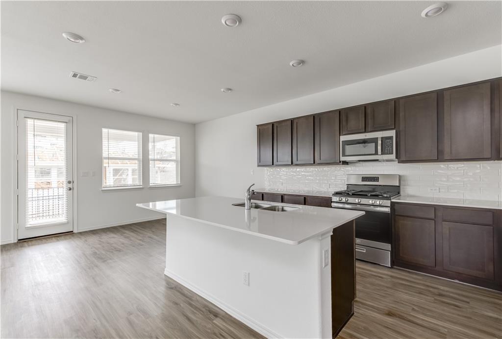 712 Affazia Lane Georgetown, TX 78628 - Photo 11 of 40 a kitchen with stainless steel appliances granite countertop a stove a sink dishwasher a refrigerator and a microwave oven with wooden floor