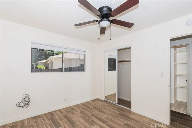 a view of an empty room with wooden floor and a ceiling fan