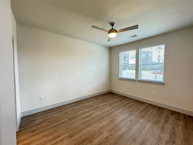 an empty room with wooden floor ceiling fan and windows