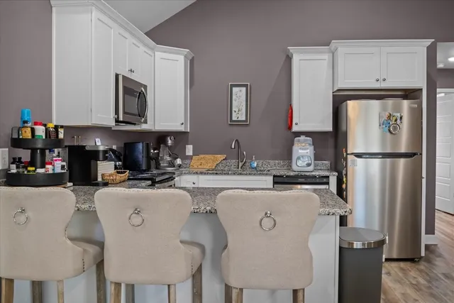 a kitchen with stainless steel appliances granite countertop a refrigerator a stove a sink dishwasher and white cabinets with wooden floor