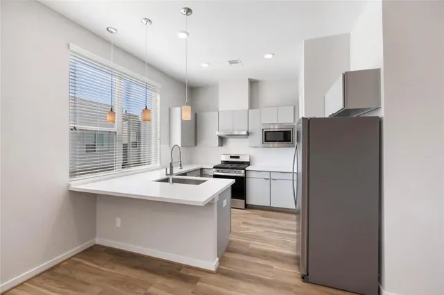 a kitchen with stainless steel appliances granite countertop a refrigerator a sink dishwasher a stove and white countertops with wooden floor