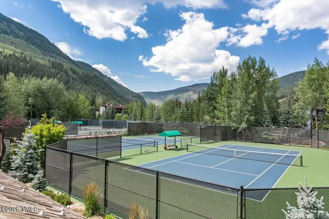 a view of a tennis ground with a table and chairs under an umbrella