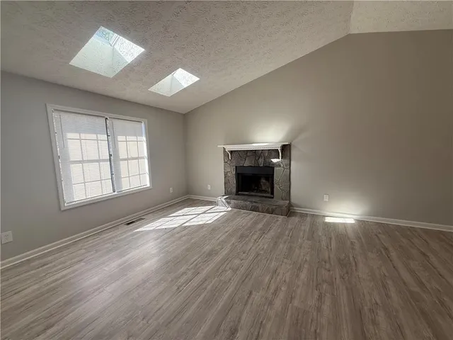 an empty room with wooden floor fireplace and windows