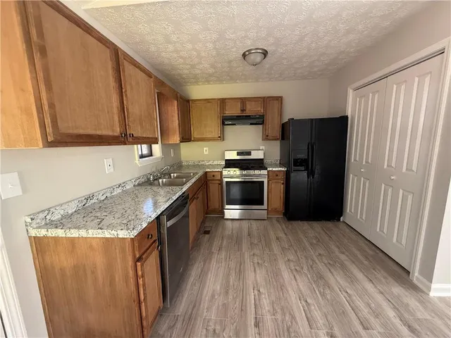 a kitchen with stainless steel appliances granite countertop a refrigerator a stove a sink and dishwasher with wooden floor