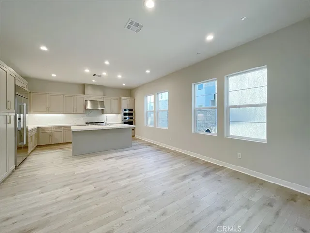 a large white kitchen with kitchen island a sink wooden floor and a view of living room