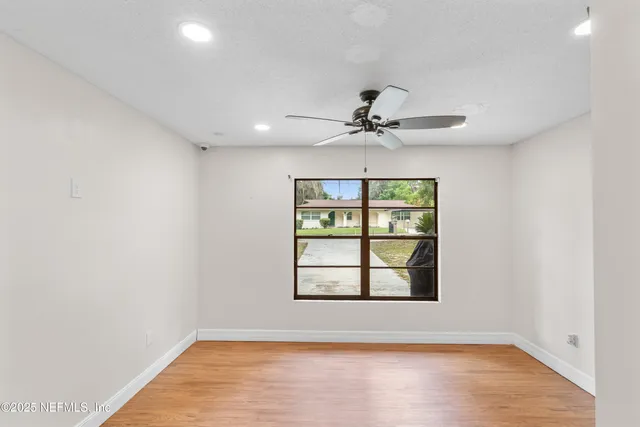 an empty room with wooden floor chandelier fan and windows