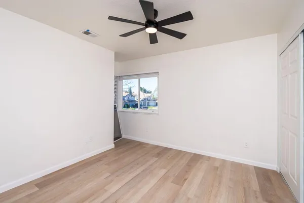 an empty room with wooden floor ceiling fan and windows