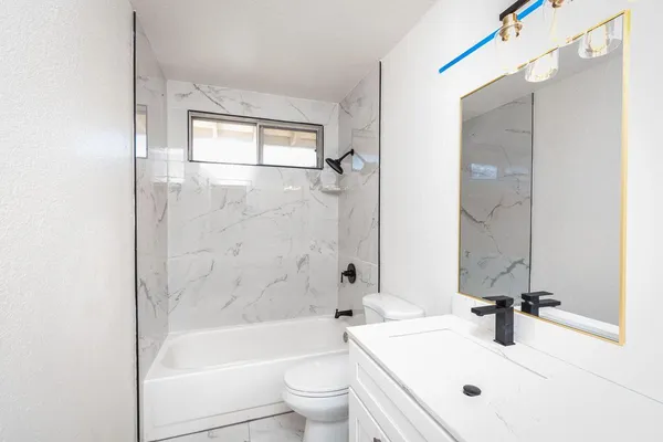 a bathroom with a bathtub shower sink vanity mirror and toilet