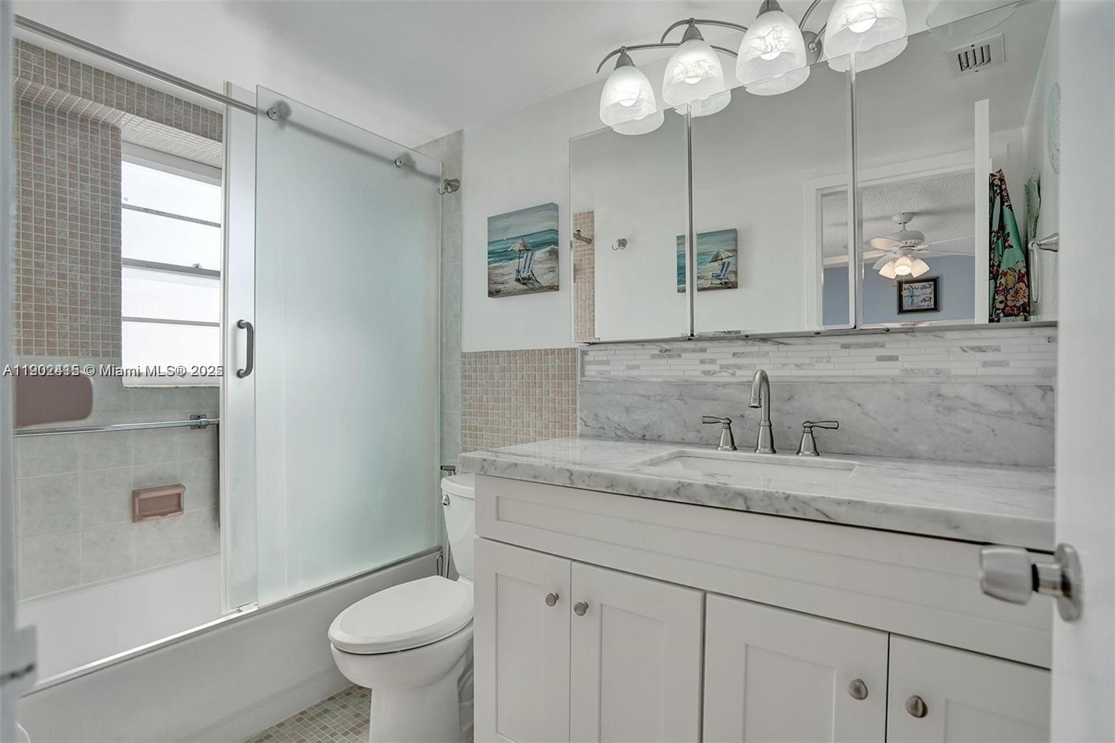7620 Carlyle Avenue, Unit 703 Miami Beach, FL 33141 - Photo 22 of 46 a bathroom with a granite countertop sink a toilet and a mirror