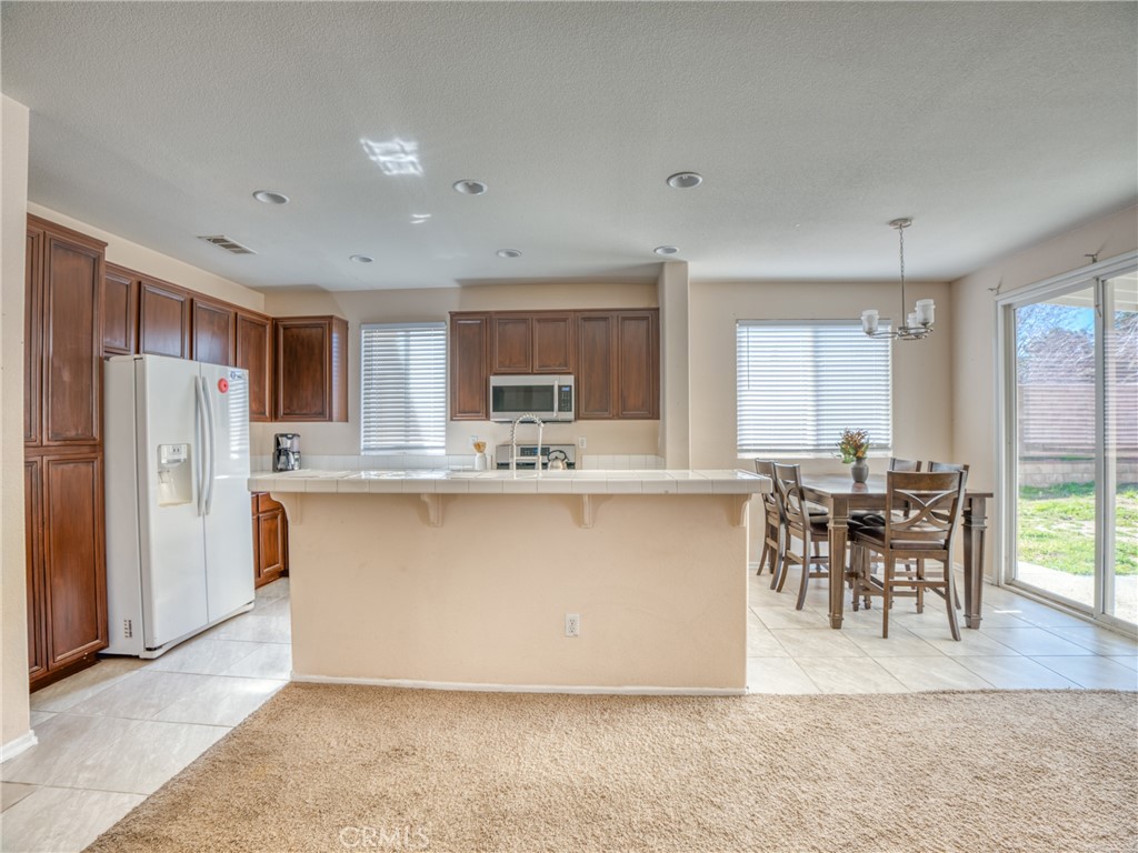 39233 Chantilly Lane Palmdale, CA 93551 - Photo 14 of 31 a living room with stainless steel appliances granite countertop furniture a refrigerator a kitchen island a stove a dining table and chairs with wooden floor