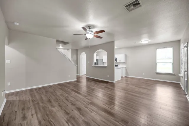 an empty room with wooden floor chandelier fan and windows