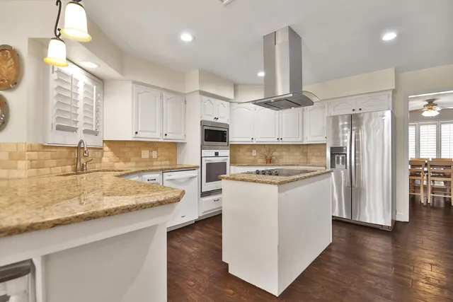 a kitchen with stainless steel appliances granite countertop a sink a stove a refrigerator and island with wooden floor