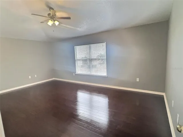 an empty room with wooden floor chandelier fan and windows