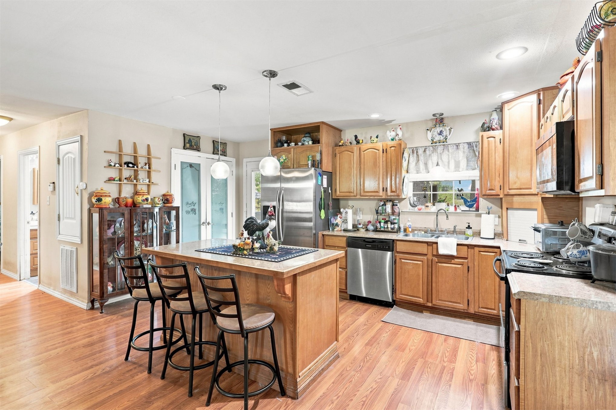 208 West Umstead Colbert, OK 74733 - Photo 13 of 25 Spacious kitchen featuring an island with casual seating, wood-finish flooring, stainless steel appliances, ample cabinetry, and a double-door pantry