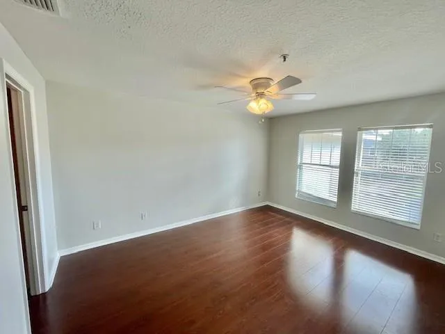 a view of an empty room with chandelier fan and wooden floor