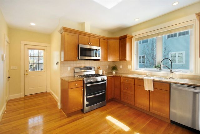 a kitchen with stainless steel appliances granite countertop a stove top oven a sink dishwasher a refrigerator and a microwave oven with wooden floor