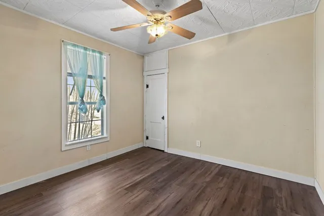 an empty room with wooden floor chandelier fan and windows