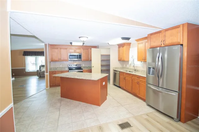 a large kitchen with stainless steel appliances kitchen island granite countertop a refrigerator and a stove top oven