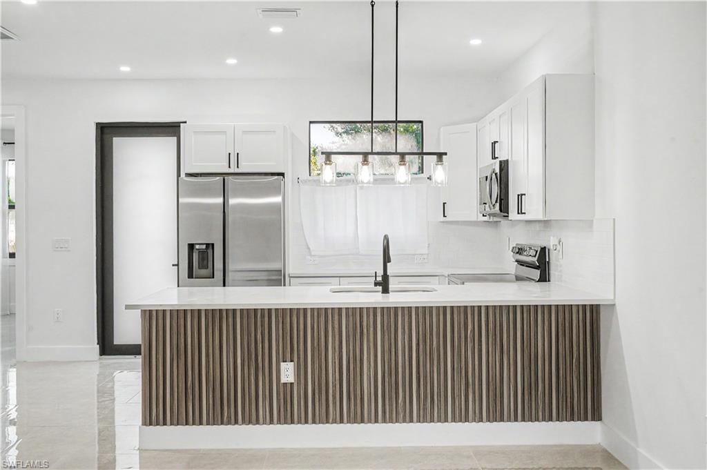 2239 Armour Road Lehigh Acres, FL 33973 - Photo 4 of 24 Modern kitchen featuring white cabinetry, stainless steel appliances, and a wood-slat island with a light-toned countertop