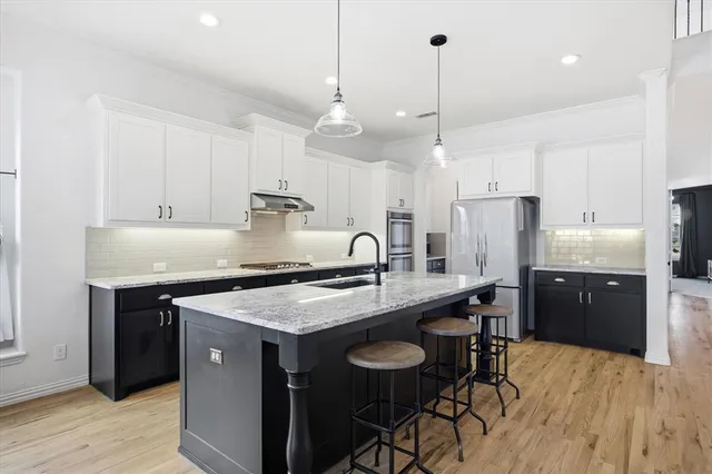 a kitchen with stainless steel appliances granite countertop a sink a stove a refrigerator and island with wooden floor