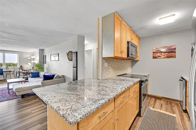 a view of kitchen island with granite countertop wooden floor white cabinets and stainless steel appliances