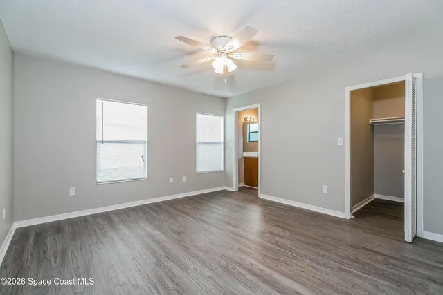 an empty room with wooden floor chandelier fan and windows
