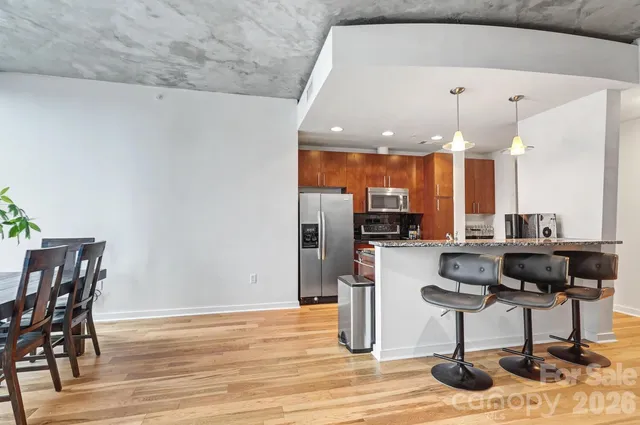 a kitchen with stainless steel appliances granite countertop a refrigerator a stove top oven a sink dishwasher and dining table with wooden floor