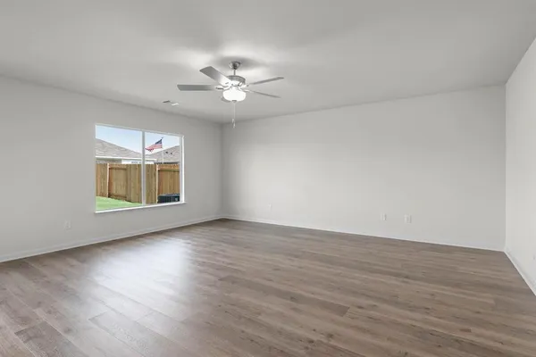 a view of an empty room with wooden floor and a ceiling fan