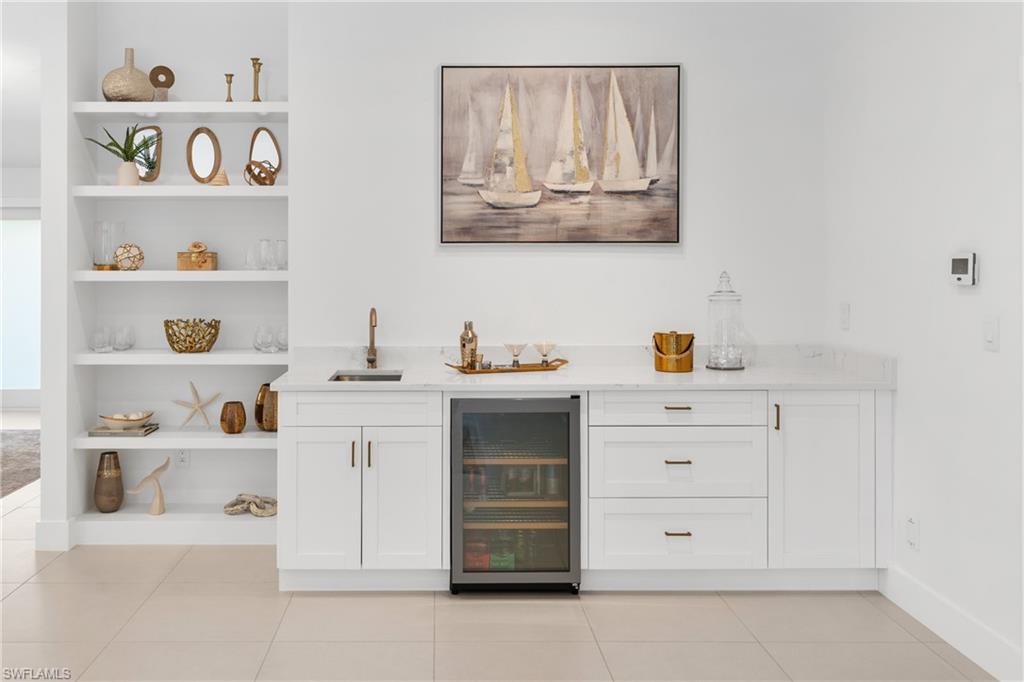 516 Neapolitan Lane Naples, FL 34103 - Photo 16 of 49 Indoor wet bar with open shelves, beverage cooler, white cabinets, light stone countertops, and light tile patterned flooring