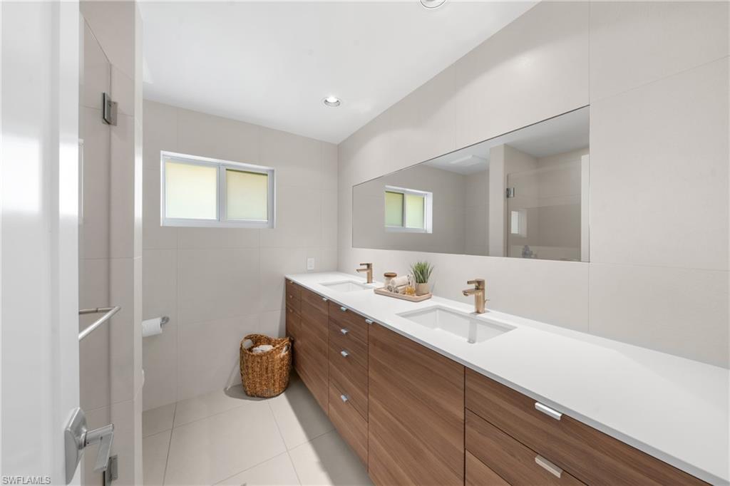 516 Neapolitan Lane Naples, FL 34103 - Photo 25 of 49 Bathroom with double vanity, light tile patterned floors, healthy amount of natural light, tile walls, and a stall shower