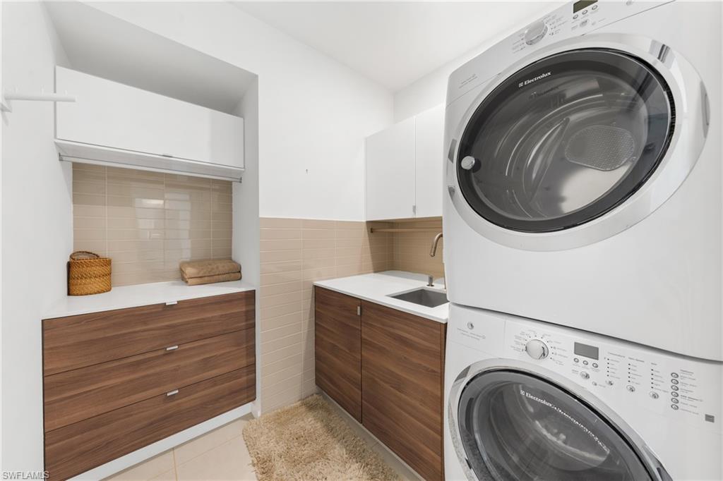 516 Neapolitan Lane Naples, FL 34103 - Photo 29 of 49 Laundry room with light tile patterned floors, cabinet space, stacked washer / drying machine, and tile walls