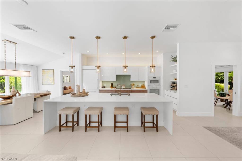 516 Neapolitan Lane Naples, FL 34103 - Photo 6 of 49 Kitchen featuring a large island with sink, white cabinetry, a kitchen breakfast bar, decorative light fixtures, and light tile patterned floors