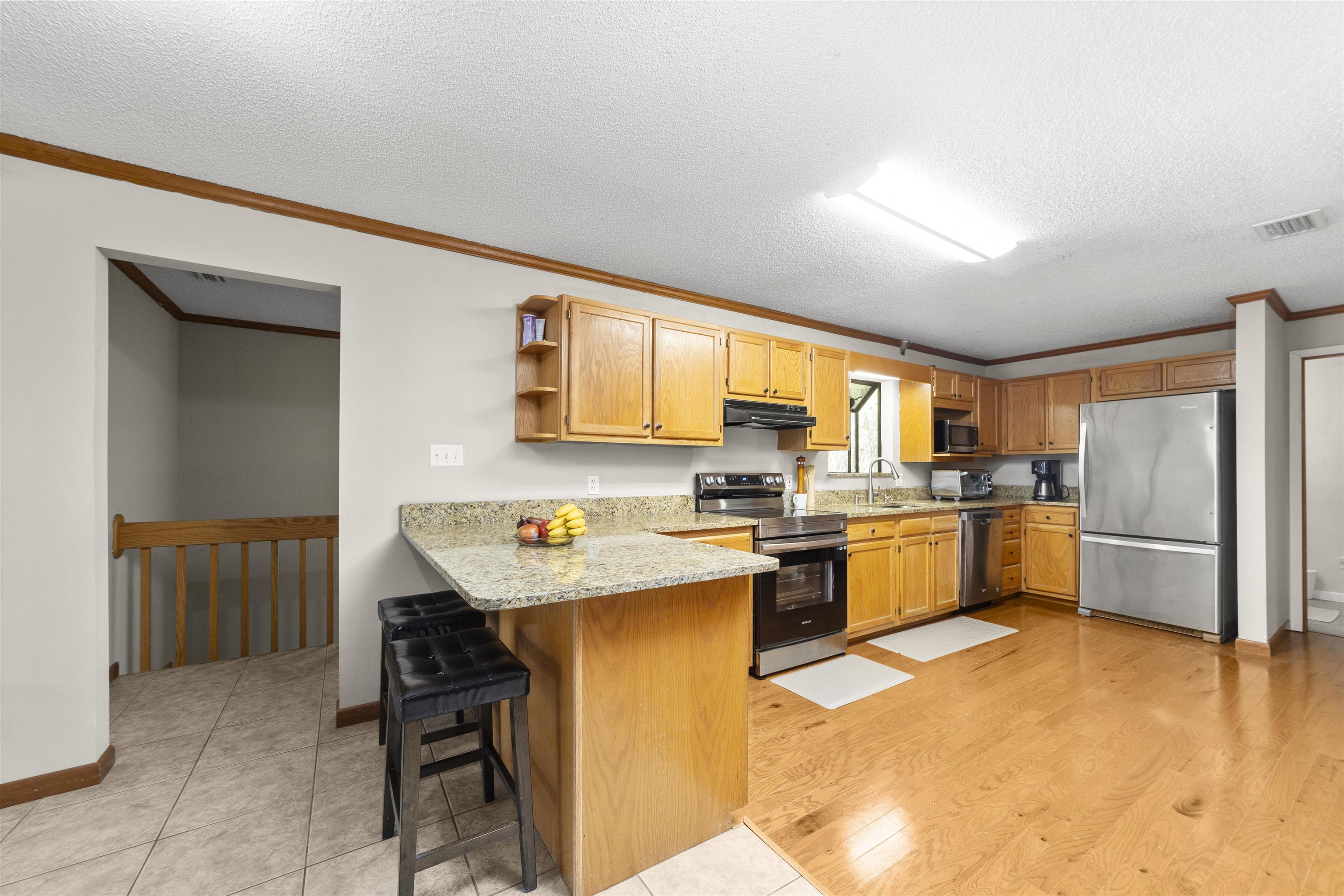 545 Ray Edwards Road St. Augustine, FL 32086 - Photo 29 of 78 Kitchen with open shelves, stainless steel appliances, crown molding, light stone countertops, and a kitchen bar
