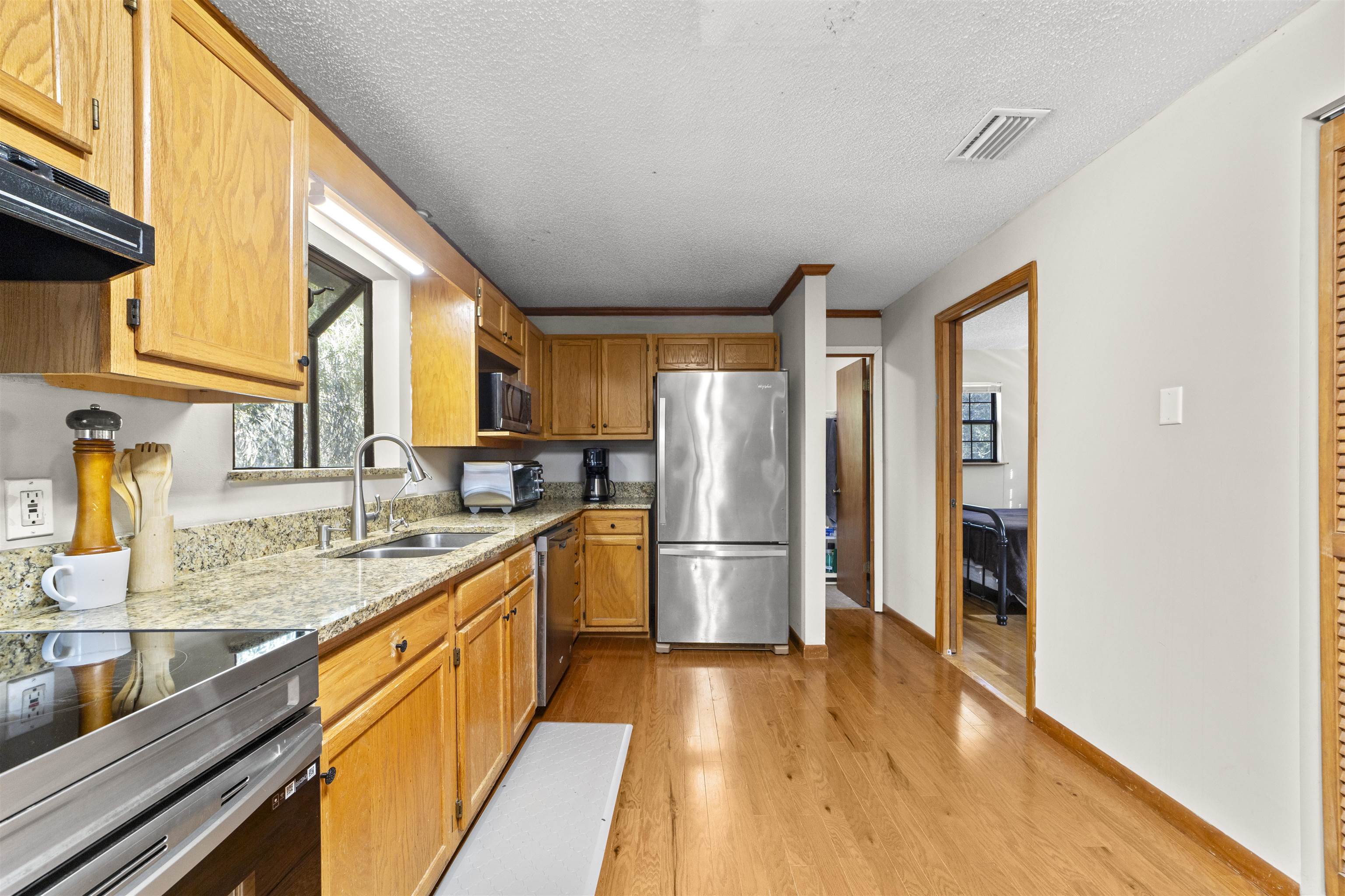 545 Ray Edwards Road St. Augustine, FL 32086 - Photo 32 of 78 Kitchen with light stone countertops, appliances with stainless steel finishes, light wood-type flooring, a textured ceiling, and brown cabinetry